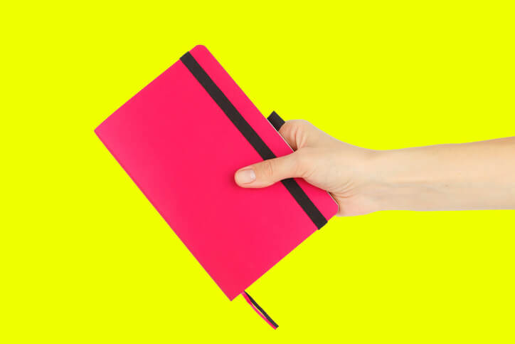 A very bright pink purse held up against a neon yellow background