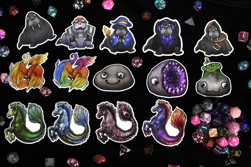 A photograph of 15 stickers, although the last one has been buried in dice of many colors, making it impossible to determine what the final sticker is. The others, in order, are walrus, MECHA-WALRUS, wizard walrus, walrumancer, and walrus rogue. Second line: Phoenix, Rainbow Phoenix, flat pet rock, geode pet rock, mossy pet rock. Third line: Emerald hippocampus, Dapple Blue Hippocampus, Lionfish Grulla Hippocampus, Twilight Hippocampus, and then the mound of dice hiding the final sticker. There are dice scattered around the edges and a few in between the stickers, showing that the die-cut stickers are each roughly 3 inches big.