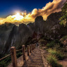 A young boy of indeterminate age beyond late-teens or thereabouts walking away from the viewer, down an ancient staircase carved into the side of a mountain.