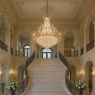 • A sweeping alabaster staircase curving gracefully beneath the glass dome of the Grand Winter Hall. • Polished marble steps catch every flicker of chandelier light, glowing softly under cascades of crystal. • Silver banisters glint like frost, guiding